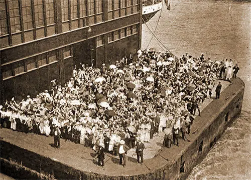 Many People Crowded Onto the End of Pier Seen From Deck of Departing Ocean Liner.